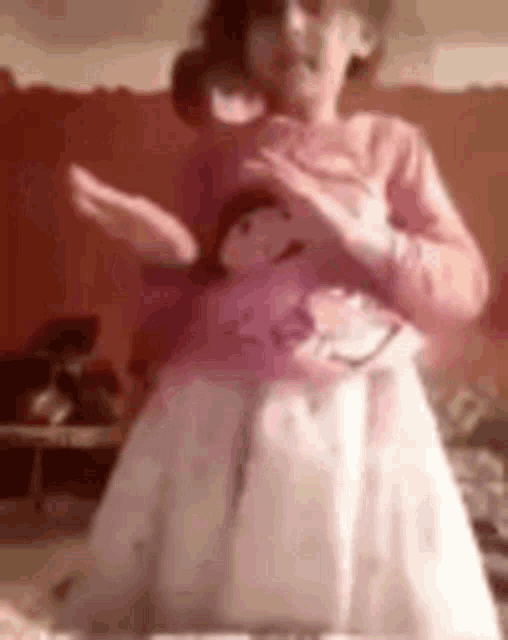 a little girl in a pink sweater and white skirt is dancing in a room .