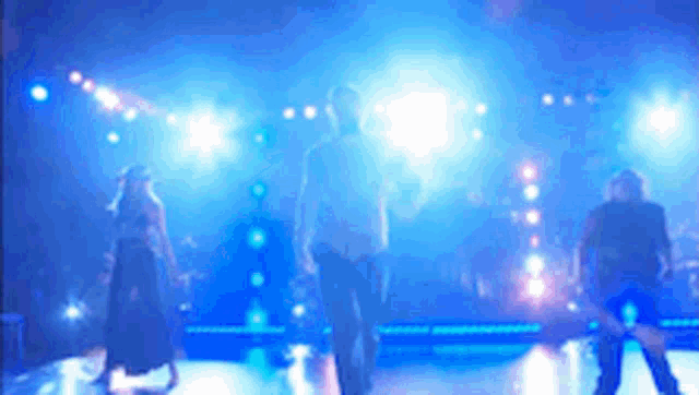 a group of people are standing on a stage with blue lights behind them