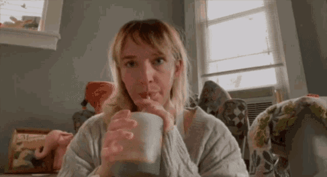 a woman is drinking a cup of coffee through a straw in a living room .
