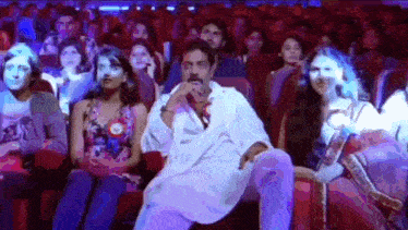 a man in a white robe is sitting in front of a crowd of people in a theater .