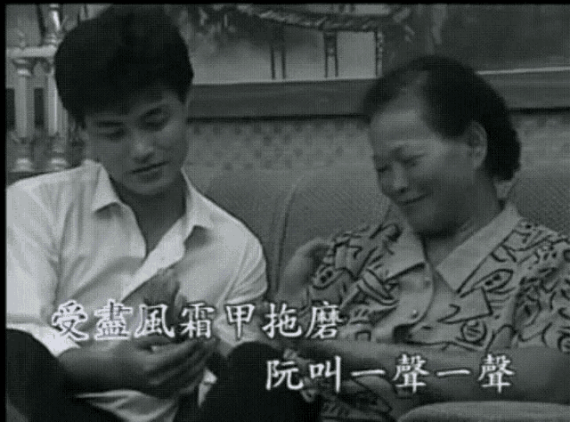 a man and woman are sitting on a couch with chinese writing on the screen behind them