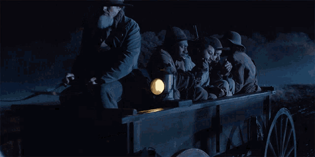 a group of men sitting in a wagon with a lantern on the back
