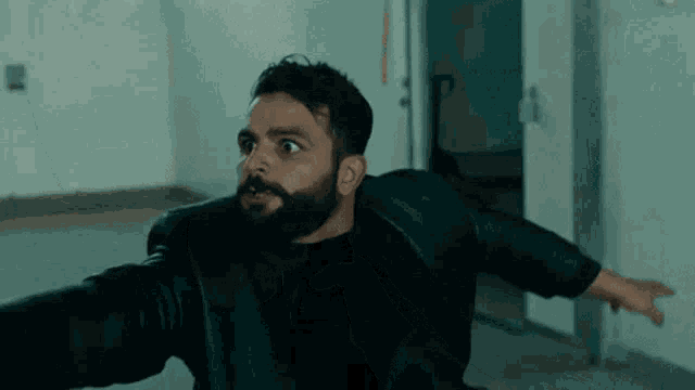 a man with a beard is wearing a black leather jacket and black shirt .