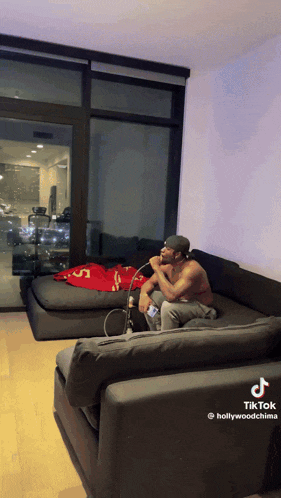 a shirtless man is smoking a hookah in a living room with a tiktok link