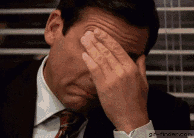a man in a suit is covering his face with his hands .