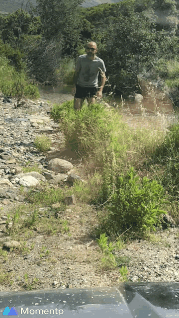 a picture of a man standing next to a river with a momento logo in the corner