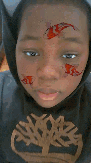 a boy with fish painted on his face wears a timberland sweatshirt