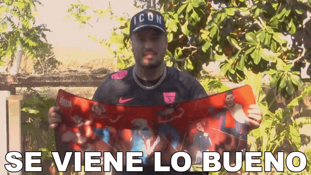 a man wearing a hat that says icon is holding a piece of paper that says se viene lo bueno