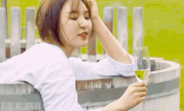 a woman is holding a glass of wine while sitting in a wooden barrel .