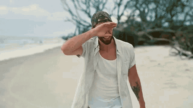 a man with a tattoo on his arm is covering his face with his hand on the beach .
