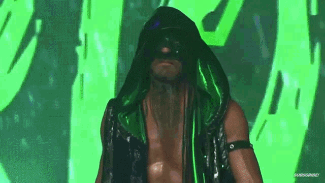 a man wearing a mask and a hood is standing in front of a green background