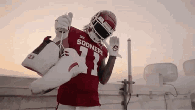a football player in a sooners jersey is holding a pair of shoes