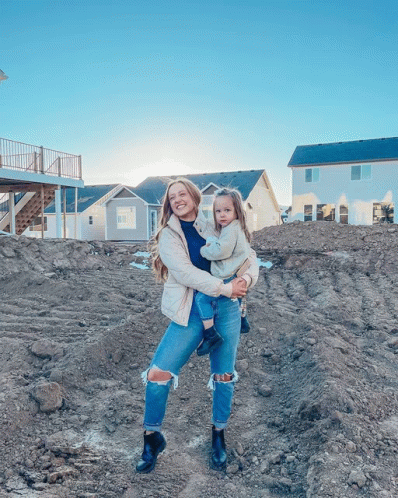 a woman holding a little girl in front of a house