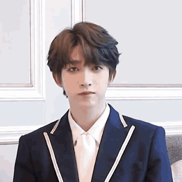 a young man wearing a suit and tie is sitting in front of a wall .