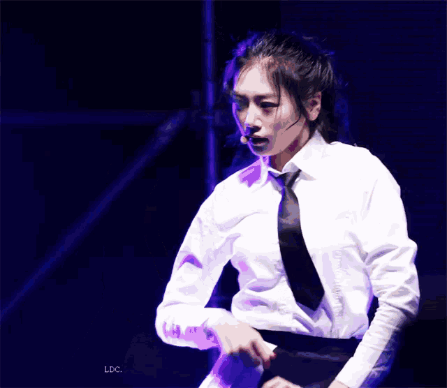 a woman in a white shirt and tie stands in front of a screen that says ldc on it
