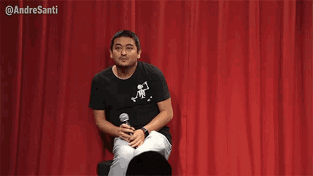 a man is sitting on a stage with a microphone in his hand .