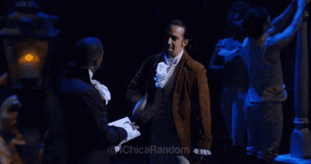 a man in a brown suit shakes hands with another man in a dark room with the words chica random on the bottom right