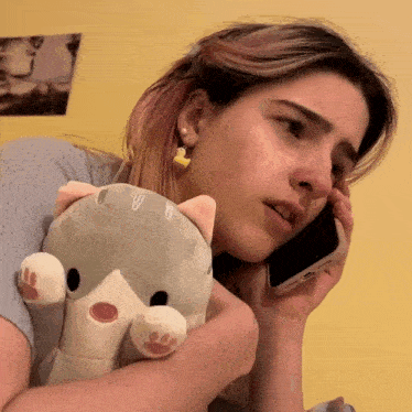 a woman holding a stuffed animal while talking on a cell phone