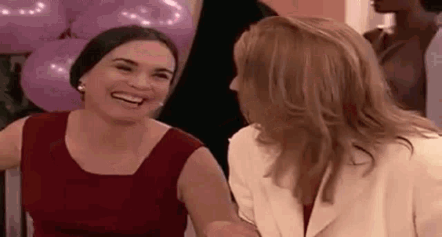 two women are laughing together at a party while sitting next to each other .