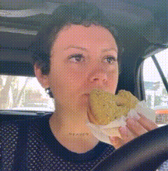 a woman is driving a car and eating a donut