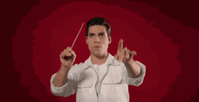 a man in a white jacket is holding a conductor 's baton in his right hand .