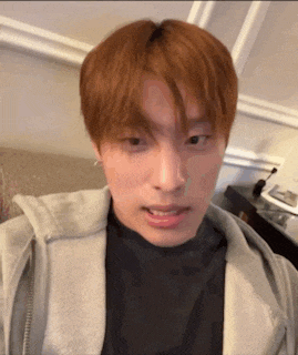 a young man with red hair is making a funny face while wearing a grey hoodie .
