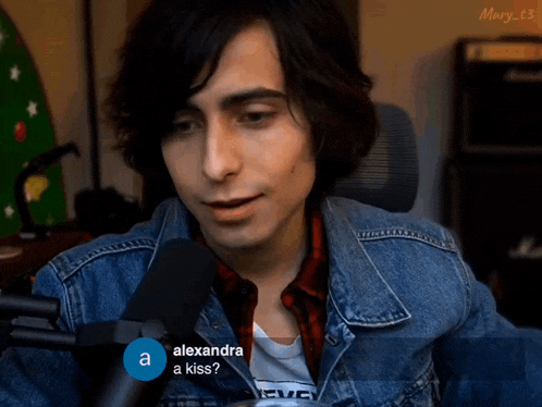 a man in a denim jacket is talking into a microphone while a blue circle says alexandra a kiss