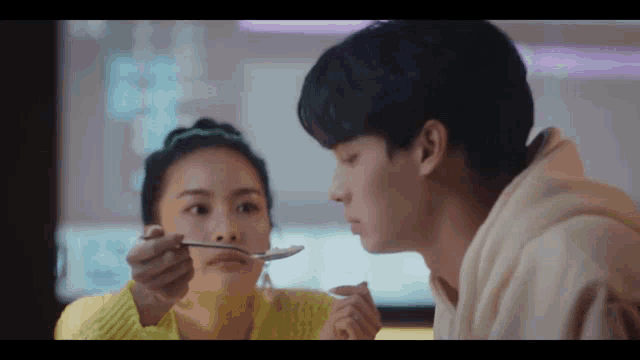 a woman is feeding a man a spoon of food .