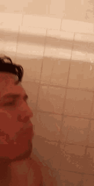 a man is taking a shower in a bathroom with a tiled wall .