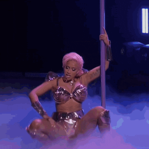 a woman is dancing on a pole in a metallic outfit