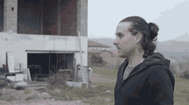 a man with long hair and a ponytail stands in front of a building