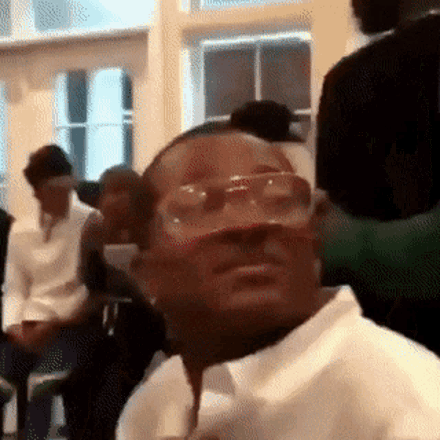 a man wearing glasses and a white shirt is sitting in a room .