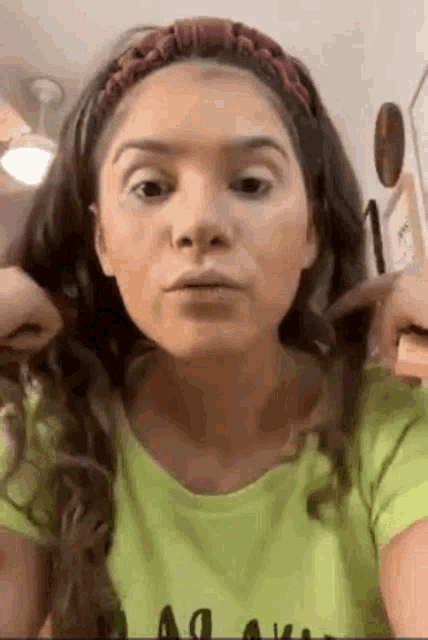 a woman is wearing a headband and a green shirt while looking at herself in the mirror .