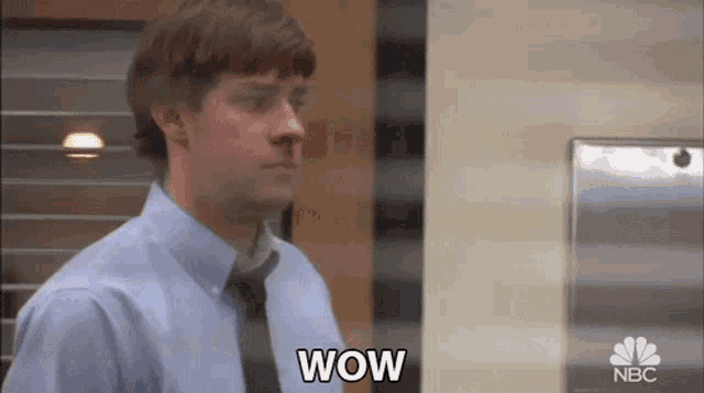 a man in a blue shirt and tie is standing in front of a refrigerator and says wow .