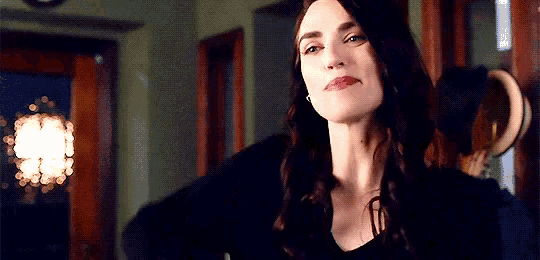 a woman with long dark hair is wearing a black shirt and earrings and looking at the camera .