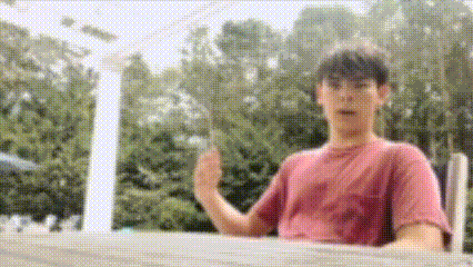 a man in a pink shirt is giving a thumbs up sign while sitting on a deck .