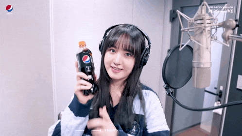 a girl wearing headphones holds a bottle of pepsi in front of a microphone