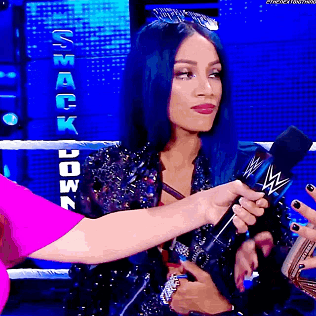a woman with blue hair is holding a microphone in front of a smack down sign