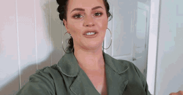 a woman in a green jacket and hoop earrings is taking a selfie .