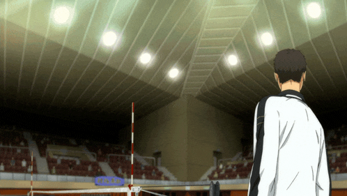 a man in a white jacket stands in a stadium with a sign that says ' volleyball ' on it
