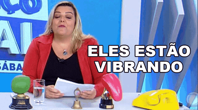 a woman in a red jacket is sitting at a table with the words eles estao vibrando