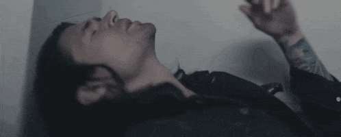 a man with long hair and a tattoo on his arm is laying down with his eyes closed