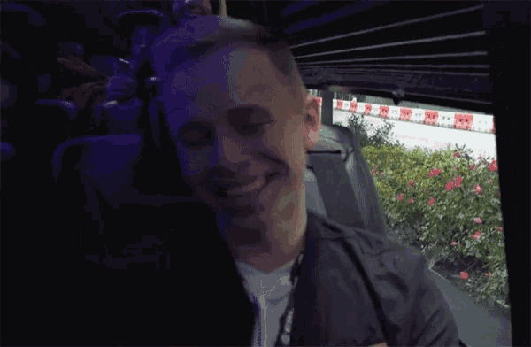 a man in a black jacket is smiling while sitting in a dark room