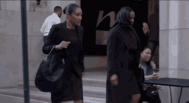 two women in black suits are walking down a street .