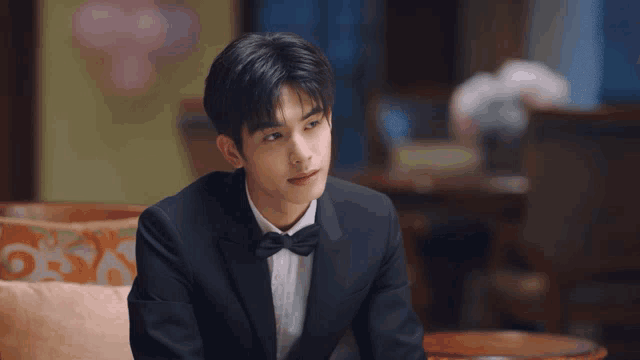 a young man in a tuxedo and bow tie is sitting on a couch