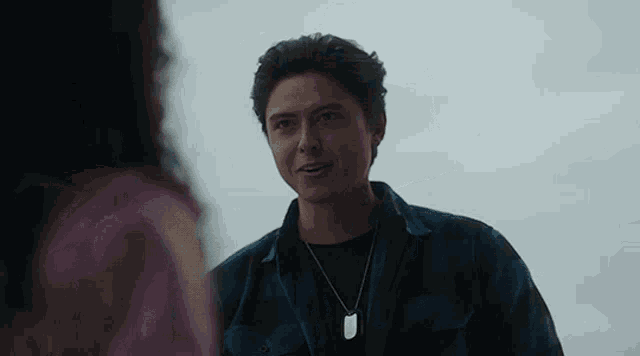 a man wearing a plaid shirt and a dog tag necklace is standing next to a woman .