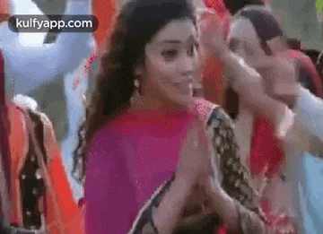 a woman in a pink saree is standing in a crowd of people and smiling .