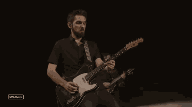 a man in a black shirt is playing a guitar in a dark room with stagemack written in the corner