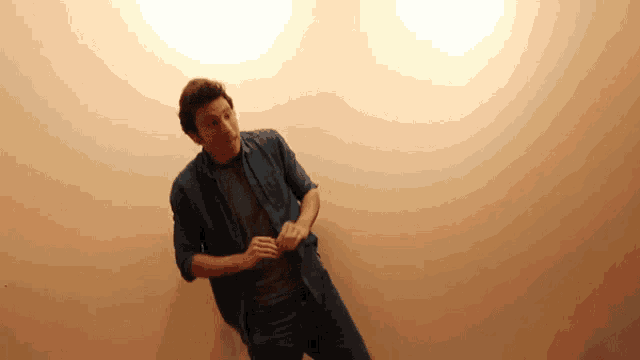 a man in a blue shirt is standing in front of a wall