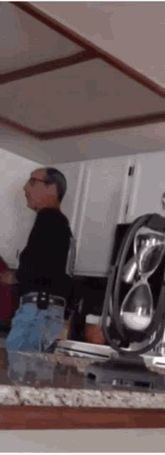 a man in a black shirt is standing in a kitchen next to a fan and sunglasses